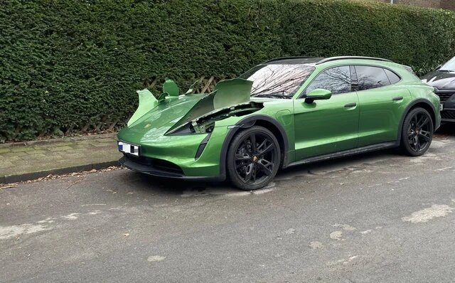 Grön bil parkerad vid trottoar med en öppen och skadad motorhuv.