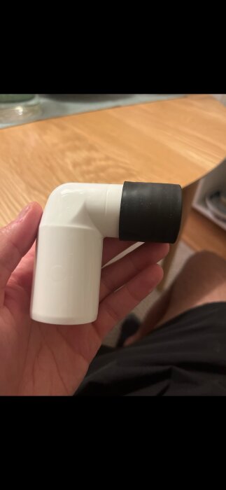 En hand håller ett vitt vinkelrör med en svart packning, troligen en del av ett avlopp.