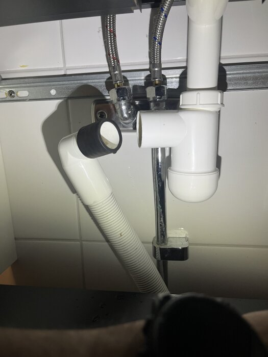 Avloppsrör under diskbänk med droppande läckage från ett rör som sätts in i ett annat. Diskussion om att använda packningstejp runt svart packning.