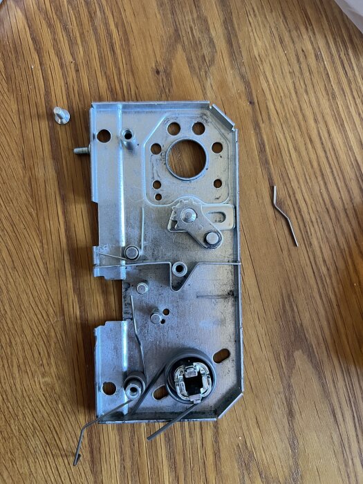 ASSA 8765 låsdel, demonterad på träbord, med lösa metallbitar bredvid.