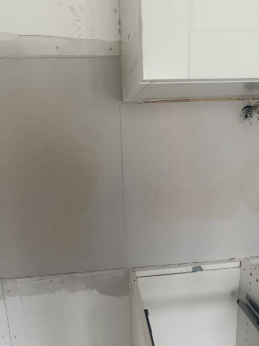 Gipsskivor utan tejpade skarvar, spacklade första gången, synliga skarvar längs vägg, överskåp i kanten av bilden.