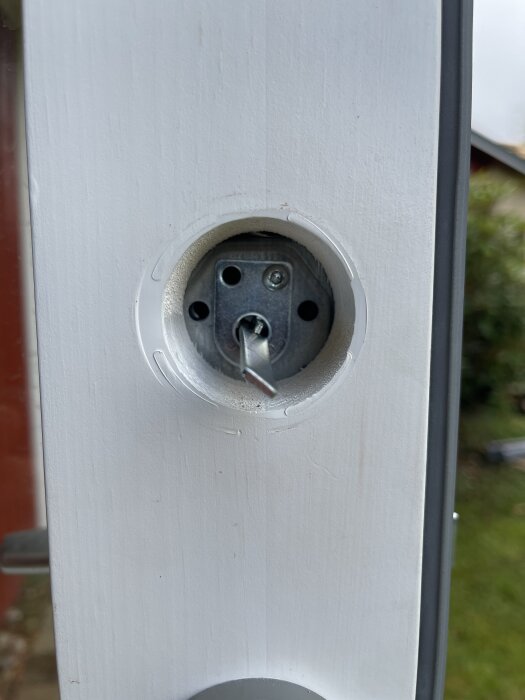 En skadad skruv i en dörrkarm, omgiven av ett avlägsnat hölje.