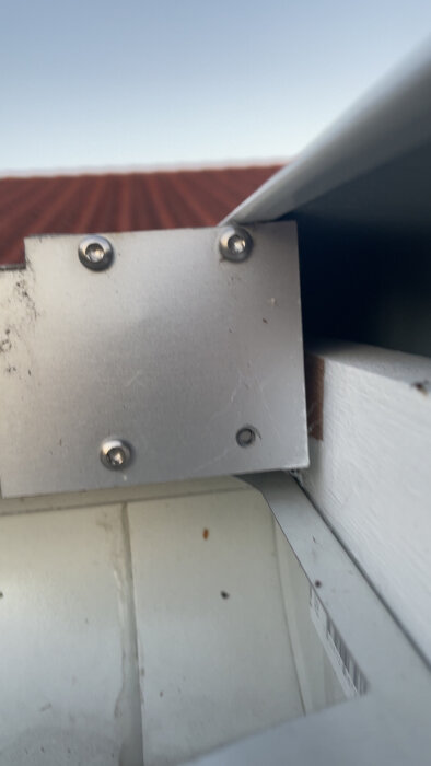 En aluminiumbit med skruvar där skruvarna inte greppar ordentligt, monterad mot en vit ram under plasttaket.