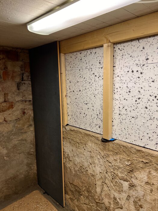 Renovering av källare med murade tegelväggar, stålreglar och isolerskivor monterade mot väggen. Takbelysning och gammal puts syns.