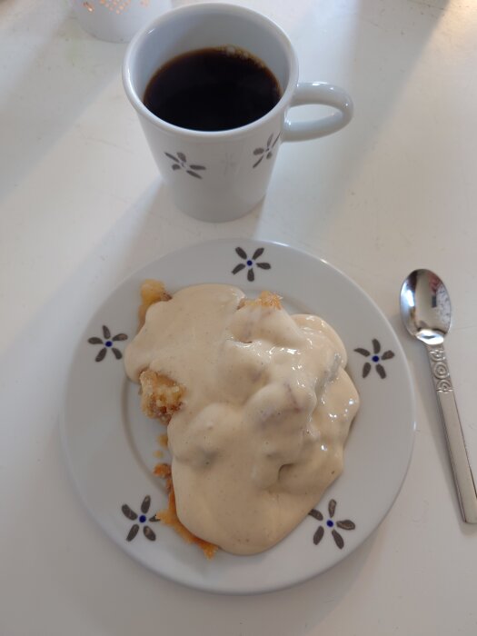 Äppelpaj med vaniljsås på en tallrik bredvid en kopp svart kaffe.