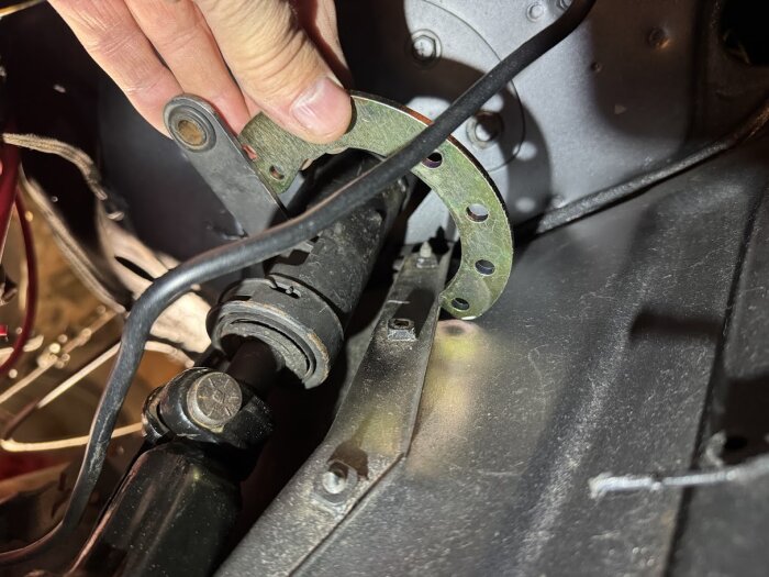 Närbild av hand som justerar en mekanisk koppling med flera skruvhål inuti en bils motorutrymme.