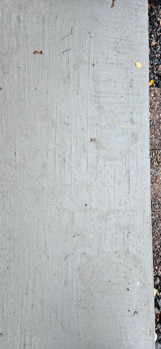 Närbild av betongyta på en förstukvist med ett randigt mönster och löv samt smuts på ytan. Grus syns längs kanten.