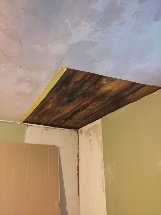 Tak med synligt hål efter läcka, delvis reparerat, gröna väggar.