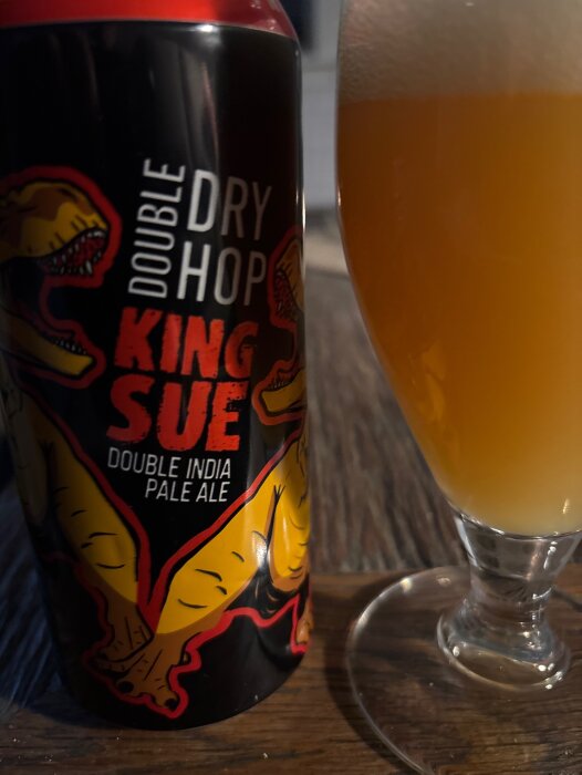 Burk med "Double Dry Hop King Sue" och ett glas med gyllene öl på ett bord.