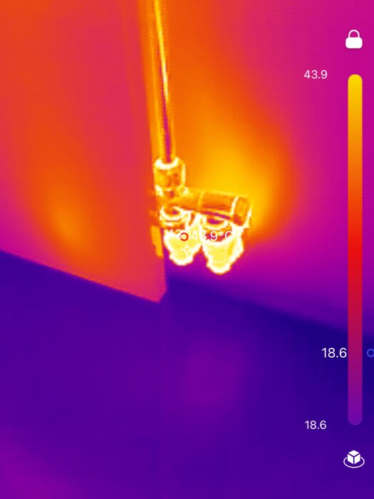 Termisk bild av rör och vägg hörn där färgerna visar temperaturvariationer, med röda och gula toner vid rören och lila vid väggen.