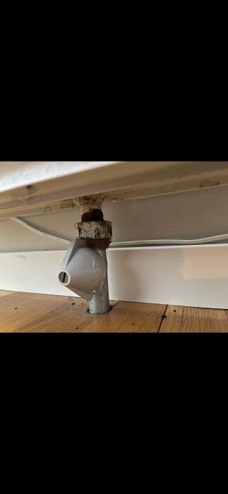 Radiatorkoppling med rostigt skikt vid muttern och en vit termostat, installation i ett 70-talshus med tidigare oljepanna, nu bergvärme.