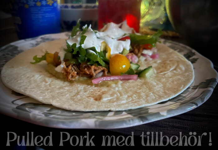 Tortilla med pulled pork, sallad, gurka, tomat och sås på en tallrik.