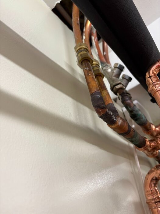 Kopparrör av olika storlekar och anslutningar i en väggöppning, med tecken på oxidation och slitage.