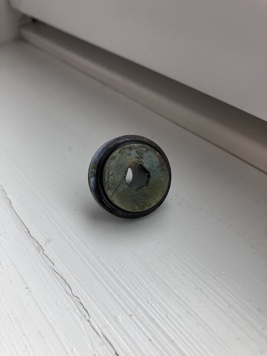 Komponent borttagen från blandare, möjligen flödesbegränsare, på vit yta.