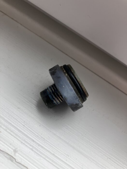 Borttagen komponent, möjlig flödesbegränsare, placerad på vit yta med skruvgängor synliga.