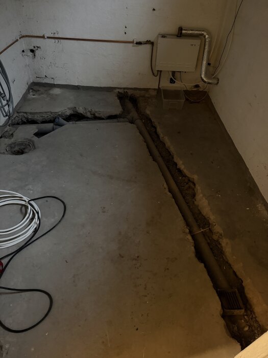 Sprucket betonggolv i källare med synliga rör och kablar. Förberedelse för flytspackling, med fokus på att minimera höjdförändringar.