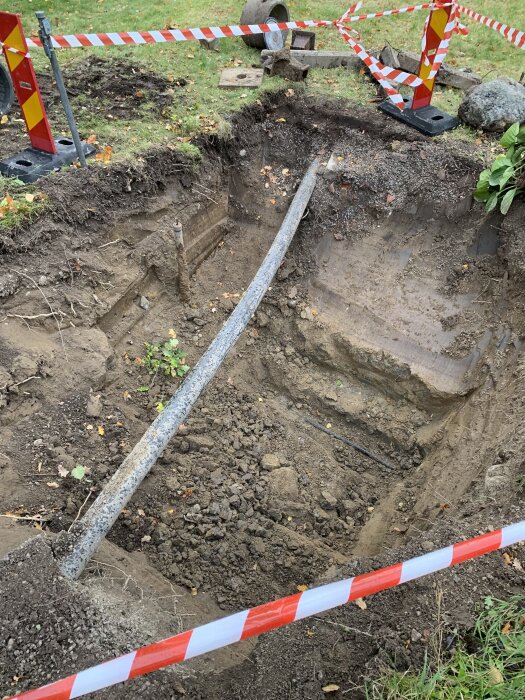 Stor grop i marken omgiven av varningsband och en avkapad metallkonstruktion, möjligen en gammal rörledning.