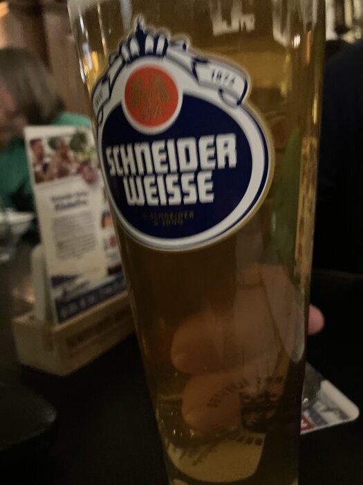 Ett glas Schneider Weisse öl på ett bord i en bar eller restaurangmiljö.