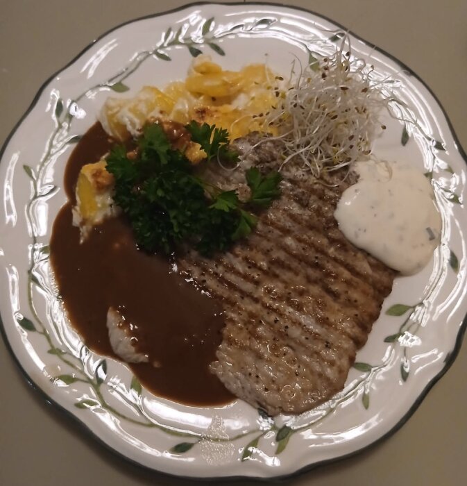 Tallrik med potatisgratäng, lövbiff, madeirasky och vispad creme fraiche med senap och västerbottenost, dekorerad med örter och groddar.