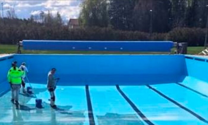 Suddig bild av en utomhuspool med arbetare och en stor rulle för pooltäcke vid kortänden på hjul eller skena.