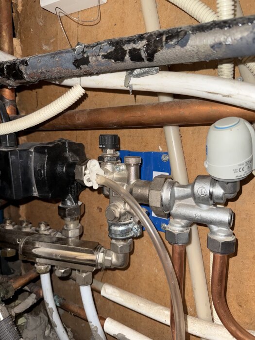 Värmesystem med rör och ventiler i ett hus, med synliga justeringsreglage och en pump utan termostat, monterat på en trävägg.