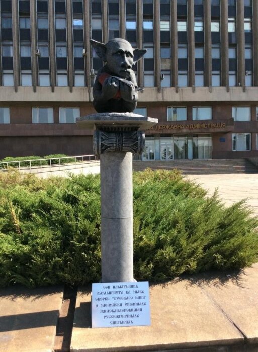 Staty av en figur med vetoformade öron och ett vapen i handen, placerad utomhus framför en byggnad.