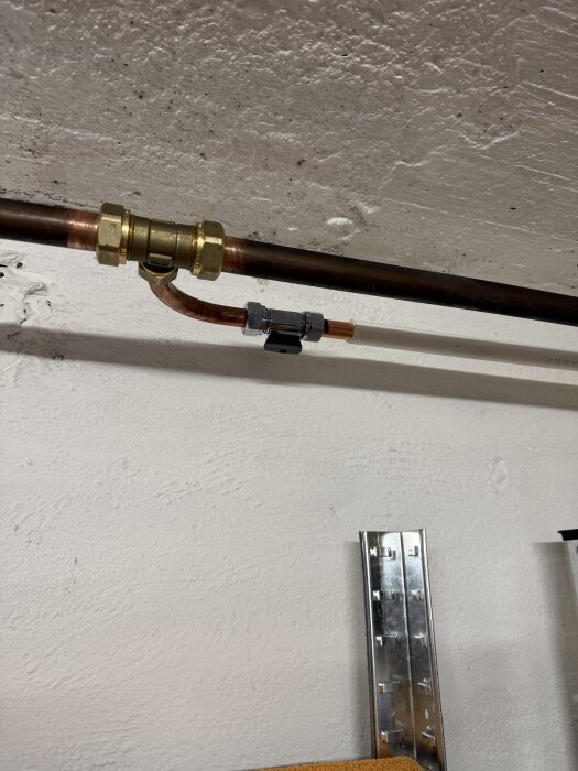 Kopparrör med ny installerad vattenutkastare på vit vägg, del av byggprojekt för att nå vatten fram på husets framsida.