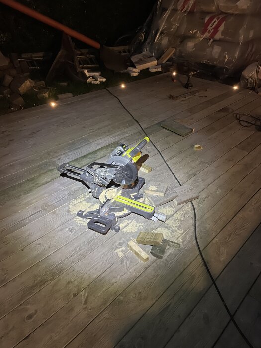 Bild tagen i mörker med pannlampa som visar kap- och geringssåg på trätrall med sågspån och virke omkring.