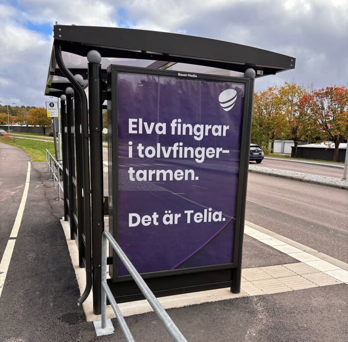 Reklamskylt vid busshållplats med texten "Elva fingrar i tolvfingertarmen. Det är Telia." mot en lila bakgrund.