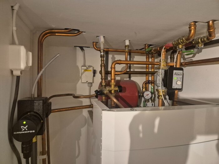 Golvvärmesystem med rör, pump och tryckmätare i ett hus.