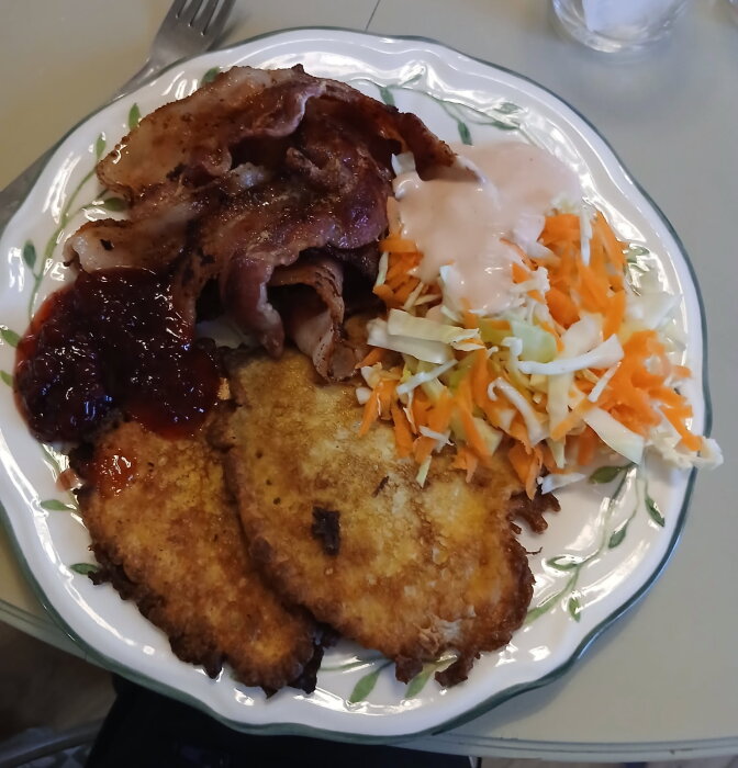 Tallrik med raggmunk, stekt fläsk, lingonsylt och råkostsallad med dressing.