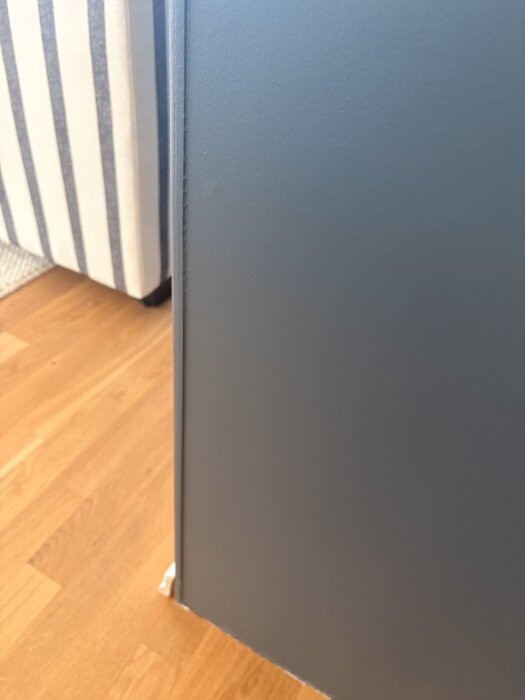 Blå skåpdörr mott en ljus trägolv med en randig soffa synlig i bakgrunden.