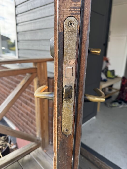 Närbild av gammalt dörrlås från märket Assa på en träfärgad dörr, med bronsfärgade handtag, under renovering.