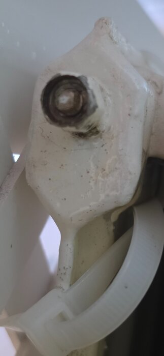 Vit skruvhuvud med rost och smuts, omgärdat av plastband. Nära vy av ett mekaniskt objekt.