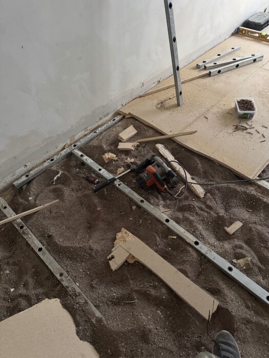 Bilden visar ett golv under renovering med avsliten spånskiva, exponerade reglar, och verktyg spridda på marken.