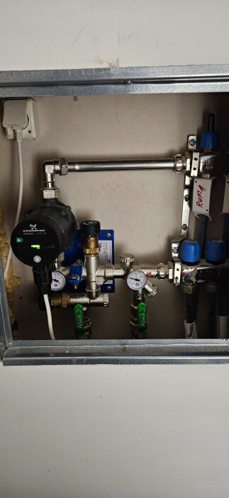 Golvvärmecentral med Grundfos Alpha2L pump, två gröna ventiler för inkommande och retur, samt manometrar och blå shuntventiler synliga.