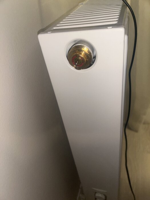 Vit radiator med ventil kopplad till en vägg.