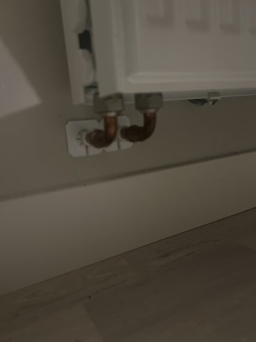 Två röranslutningar på en radiator under installation, metallrör går in i väggen, del av värmesystem.