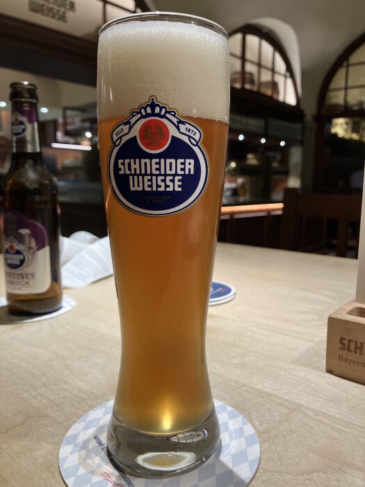 En ölglas fyllt med Schneider Weisse öl på ett bord, med en flaska i bakgrunden.