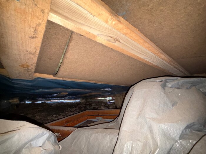 Under huset, där tillbyggnaden är, hängande och glipande strukturer med träreglar och plastduk synliga. Möjliga tecken på fuktproblem.