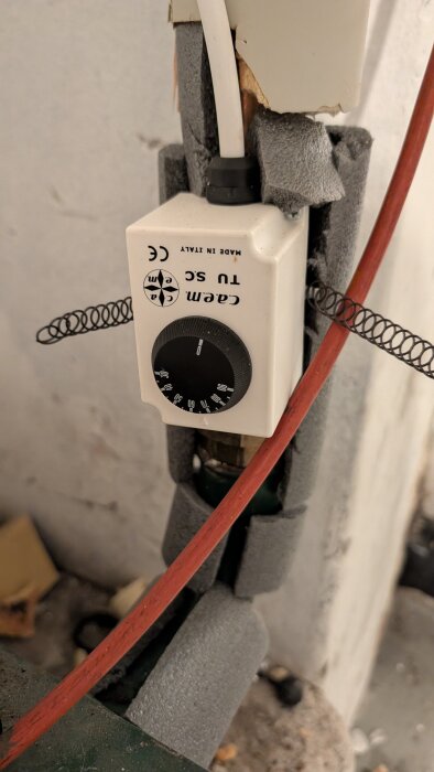 Termostat monterad på rör, styr cirkulationspump för laddomat, inställd på 65 grader, vita och röda kablar synliga.