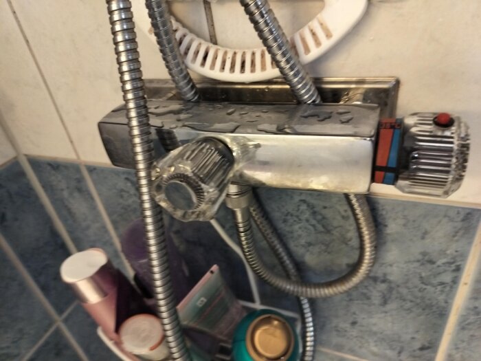 Duschblandare med vridknappar och duschslangar mot kakelvägg, närbild från badrum.