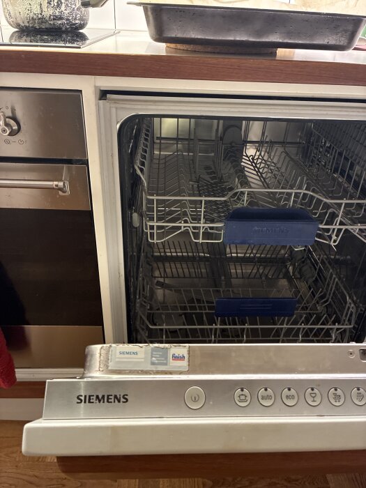 Öppen Siemens diskmaskin i ett kök med tomma trådkorgar, kontrollpanel och synlig köksbänk ovanför.