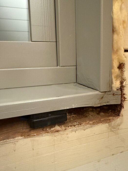 Fönsterinstallation med borttagen karm visar fuktrelaterad skada under fönstret, synlig tejp och avrinningsplåt, omgiven av isolering.
