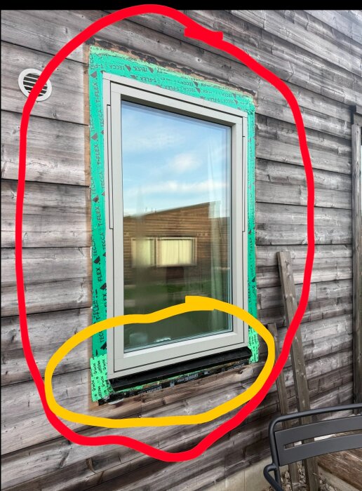 Fönster omgivet av röd markering; potentiellt fel inom gul cirkel under fönstret vid en trävägg med grönt tejp runt om.
