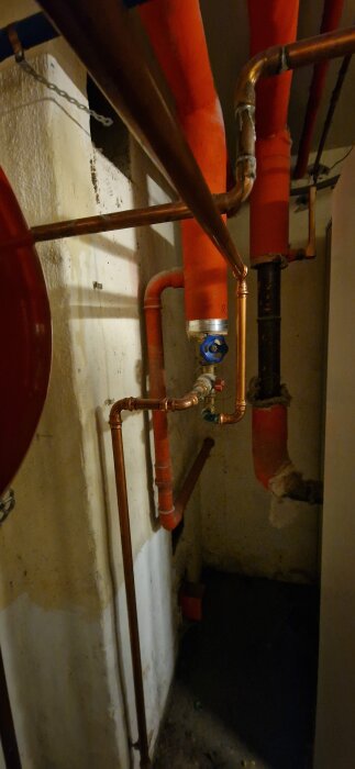 Rörsystem med koppar- och isolerade rör samt ett blått vred i en källare, del av ett bergvärmesystem.