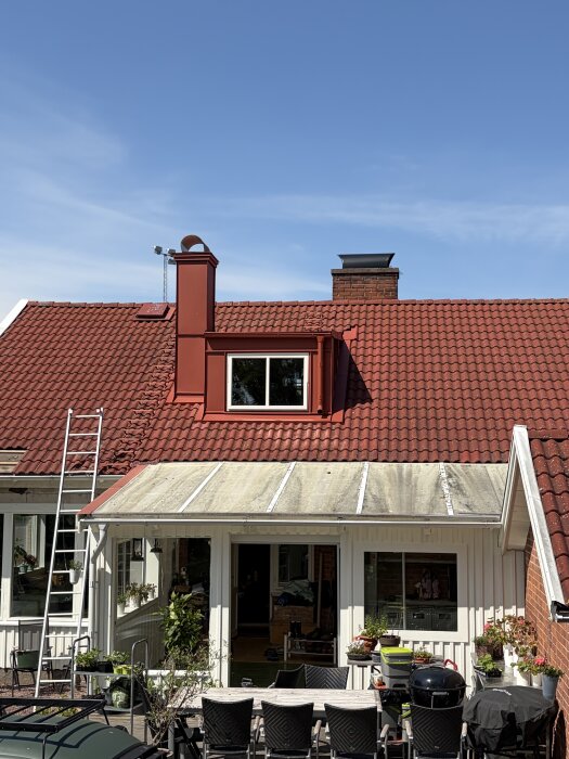 Rött hustak med en stege som leder till en taklucka, används för att nå vinden utifrån.