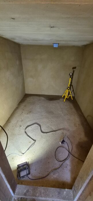 Renoveringsprojekt i rum med slammade och grovputsade väggar, golv med sladdar och belysning; förberett för eldragning och installation av Tylö 8kW.