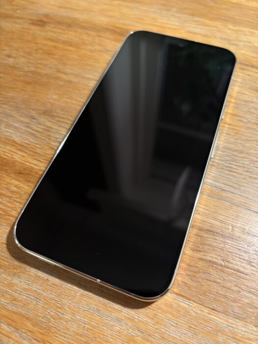 Smartphone med svart skärm på ett träbord.