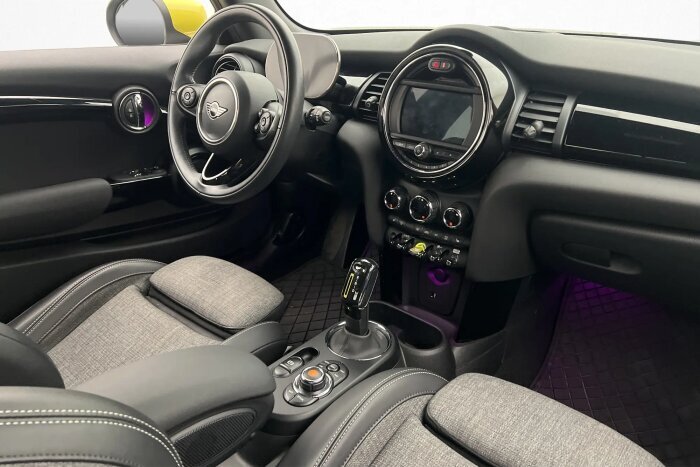 Interiören i en Mini F56 elbil med klassisk design, flyplansliknande brytare, ratt och kontrollpaneler för värmesystem och sätesvärme.